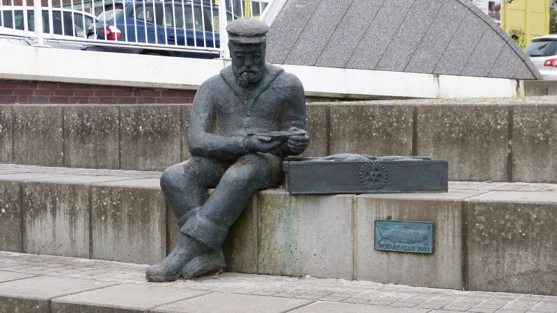 Bronzeskulptur eines Fischers mit Fischkiste am Hafen